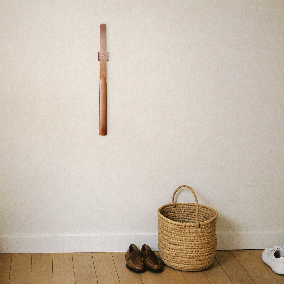 Wooden shoehorn mounted on the wall above an entryway basket and leather loafers